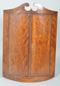 An early 19th century mahogany hanging corner cupboard, of D-section, with swan neck pediment,