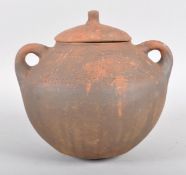 An African terracotta two handled globular jar and cover, incised with waves and liner bands,