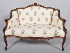 A late Victorian mahogany two seat sofa, the frame carved overall with scrolls and swags,
