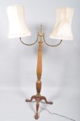 An Edwardian mahogany double standard lamp having brass sweeping arms and finial top on an urn