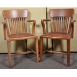 A pair of early 20th Century oak elbow chairs having rail backrests, shaped armrests,