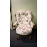 An Ercol style wide armchair having a spindle backrest, shaped arms and raised on shaped legs,