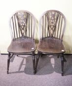A pair of 20th Century wheelback dining chairs having saddles seats and raised on turned legs.