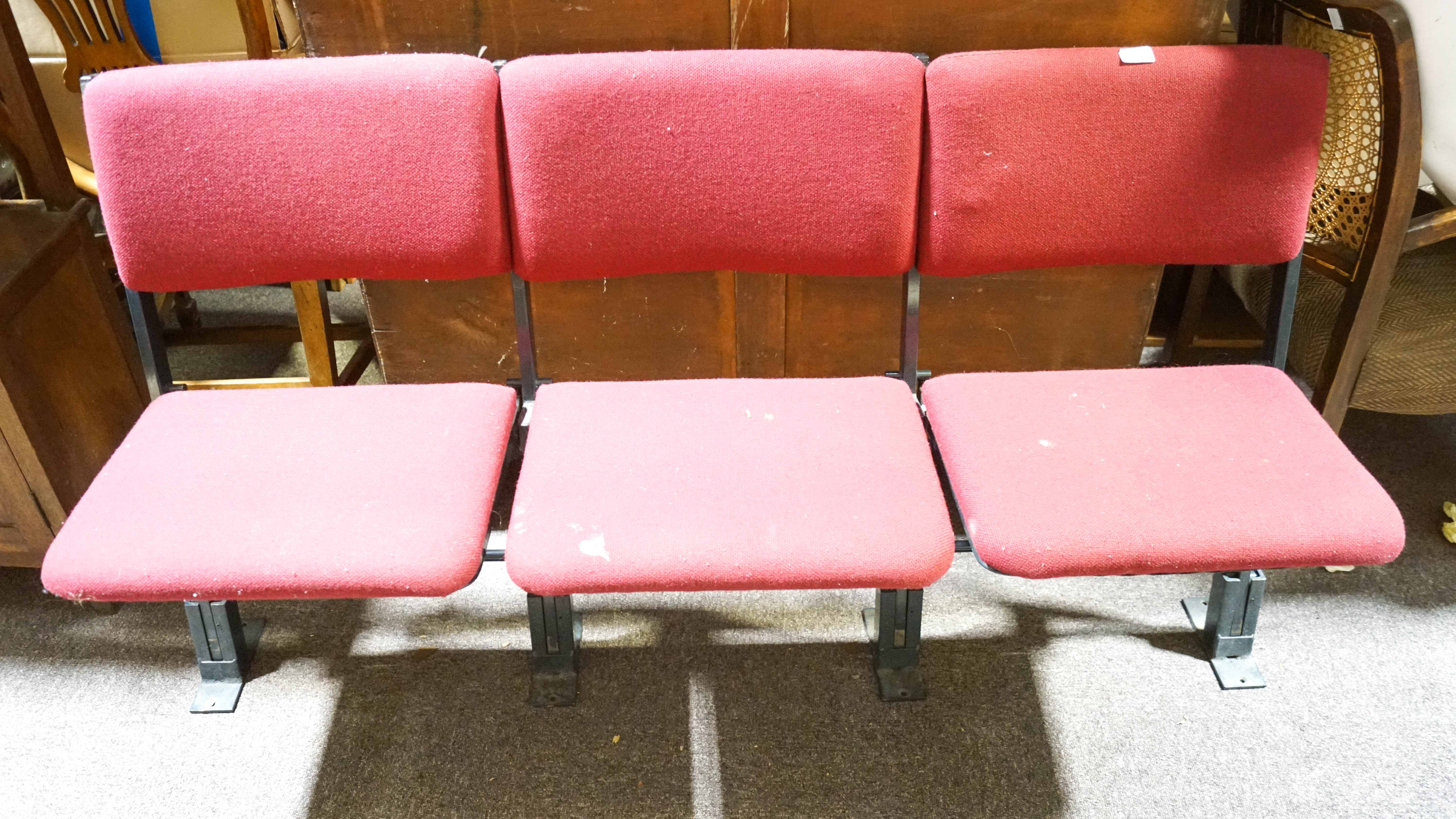A set of three theatre/events folding chairs having a black metal frame with red upholstered