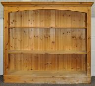 A pine bookcase having a flared top, two shelves and raised on a plinth base.