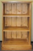 A 20th Century pine bookshelf having a flared top, two shelves and raised on a plinth base.