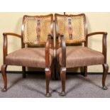 A pair of Edwardian oak open armchairs having bergere cane work back rest and deep cushioned seat,