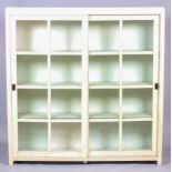 A modern cream painted glazed bookcase, with sliding panelled doors, enclosing three shelves,