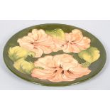 A Moorcroft 'Peach Hibiscus' pattern circular dish on a green ground,