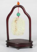 A Chinese carved pale celadon jade pendant and hardwood stand, of oval form,
