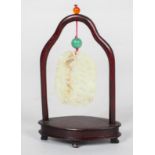 A Chinese carved pale celadon jade pendant and hardwood stand, of oval form,