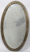 An Arts & Crafts hammered brass oval mirror frame, with oak leaves on a textured ground,
