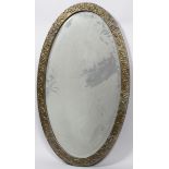 An Arts & Crafts hammered brass oval mirror frame, with oak leaves on a textured ground,