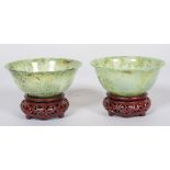 A pair of Chinese carved translucent green spinach jade bowls and hardwood stands, 20th century,