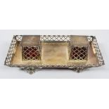 A silver desk standish, of rectangular form with angled pierced sides and raised on scroll feet,