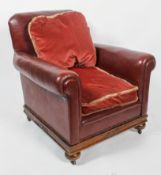 An early 20th century red leather Club armchair, with red velvet drop in cushions, with scroll arms,