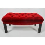 A George III style ebonised foot stool, the button back top upholstered in cherry red velvet,