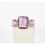 A yellow metal ring set with three graduated rectangular cut amethyst