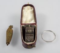 A collection of items: A Platinum wedding ring, a gold plated sarcophagus; a silver scarf buckle