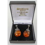 A white metal pair of drop earrings having a leaf design and fixed with reconstructed amber