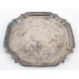 A silver salver, of cut cornered square design with fancy border, raised on four scroll feet,