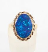 A yellow metal ring set with an oval cabochon cut synthetic black opal. Hallmarked 9ct gold, London.