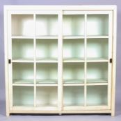 A modern cream painted glazed bookcase, with sliding panelled doors, enclosing three shelves,