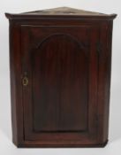 A George III oak corner cupboard with frieze top over an arch panelled door,