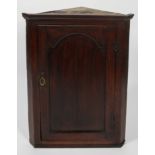 A George III oak corner cupboard with frieze top over an arch panelled door,