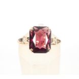 A yellow metal single stone ring. Set with a rectangular cushion cut rhodolite garnet.