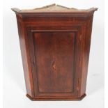 A George III oak inlaid corner cupboard, with a dentil cornice below panelled door,