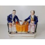 A Victorian Staffordshire pottery figure group - two men holding hands at a table whilst smoking,