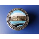 An embossed circular Swedish silver pill box, the hinged cover enamelled with a view of Stockholm,