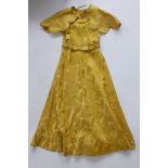 A 1930's Chinese gold silk damask dress with matching cape decorated with gilt braid.