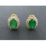 A modern pair of oval emerald & diamond cluster earrings, each emerald weighing approximately 2