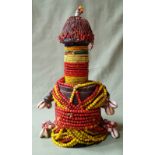 An African stylised doll figure encased by strings of yellow & red coloured glass beads and with