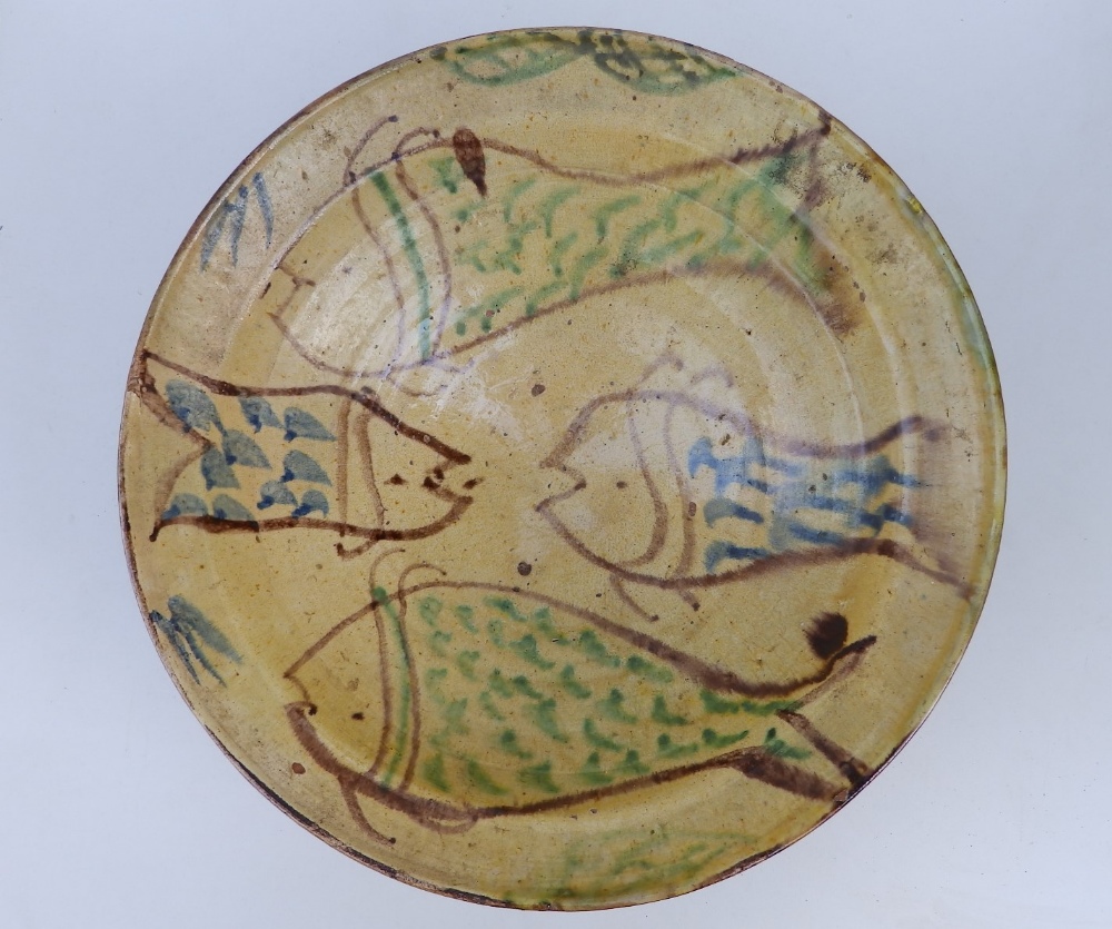 A large old studio pottery bowl, decorated with four stylised fish on a pale yellow ground, unglazed