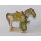A Tang partially glazed pottery figure group depicting a saddled horse with its attendant, on a