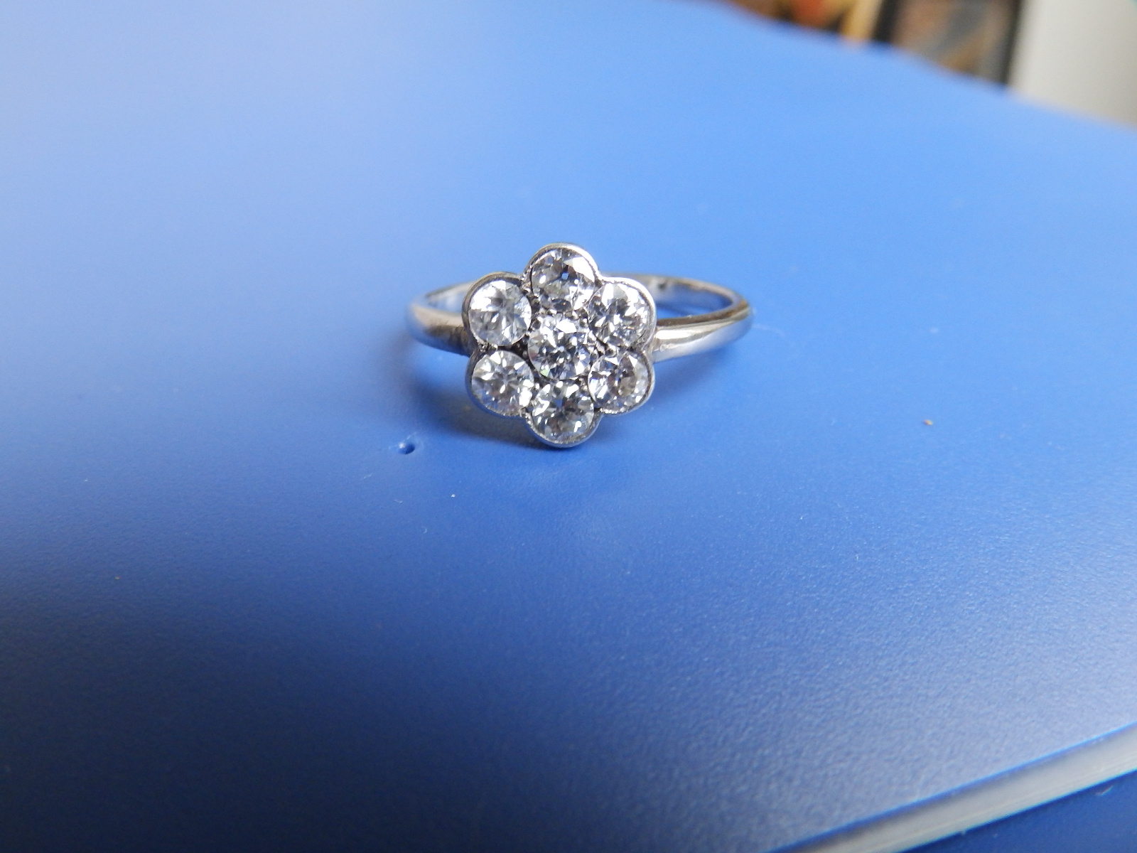 A diamond daisy cluster ring in white metal. Finger size O/P.