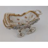 An early 20thC German porcelain model pram, painted flowers with gilding, on slender rotating