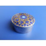 A circular white metal trinket box, the domed detachable cover enamelled in a stylised floral