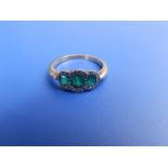 A small three stone emerald ring with diamond borders on yellow metal shank. Finger size O.