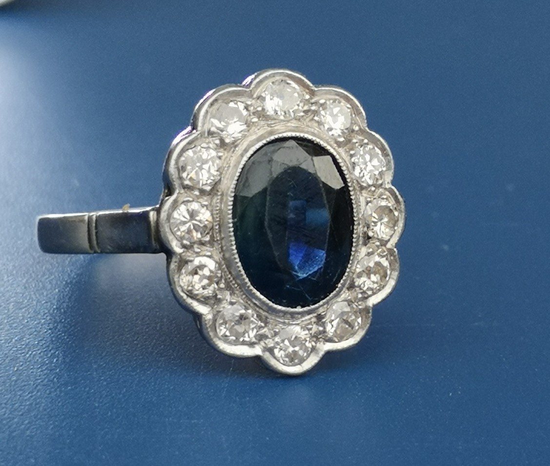 An oval sapphire & diamond millegrain set cluster ring, the sapphire weighing approximately 2.75