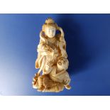 A Japanese Meiji period ivory okimono carving depicting a man beating on a drum held by an angel,