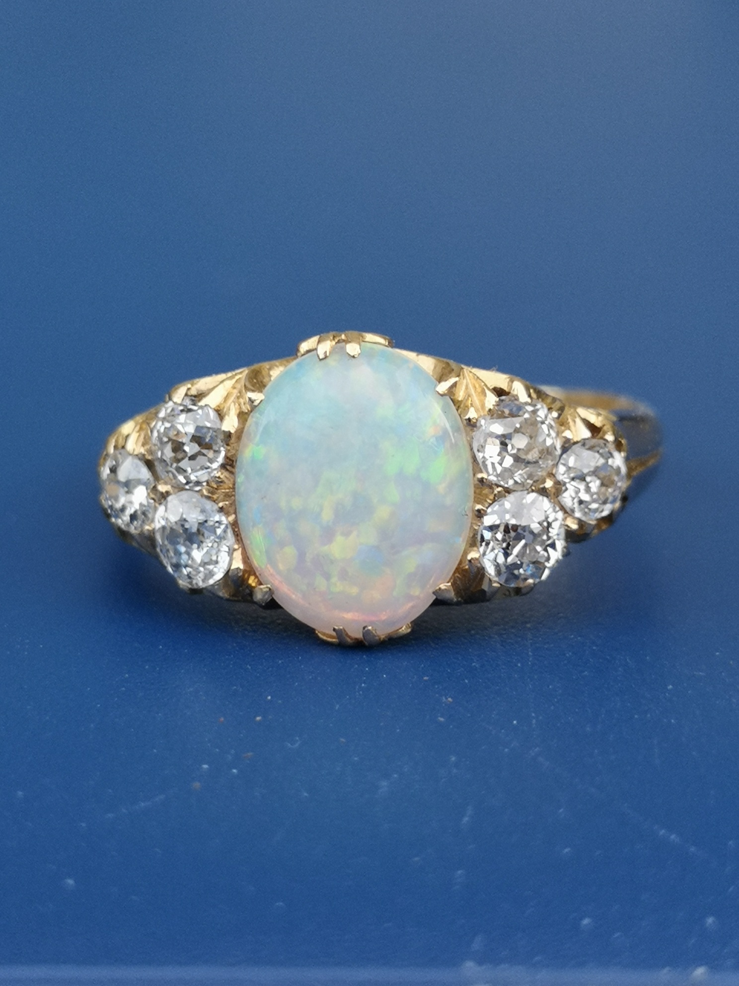 An opal & diamond set 18ct gold ring, the oval claw set opal flanked by six old cut diamonds. Finger