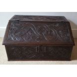 An antique carved oak table top slope front desk, decorated with mythical beasts and birds with
