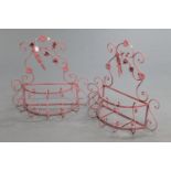 A pair of wrought iron pink painted garden planters, with floral and scrollwork decoration.