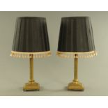 A pair of brass table lamps with shades, each with Corinthian capital.