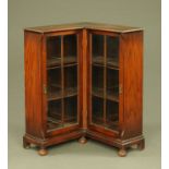 A 1930's oak corner bookcase, with glazed panelled doors to fixed shelves and raised on bun feet.