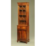 A reproduction mahogany narrow bookcase, the base fitted with a drawer, slide and cupboards.